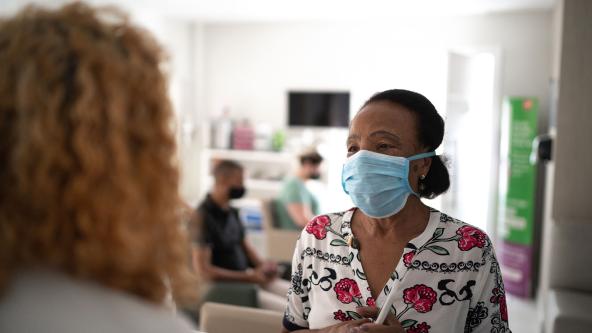 A masked patient talking to a receptionist. 