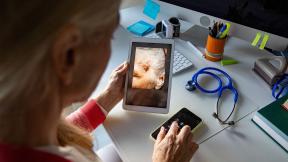 A GP holding a video call appointment and looking at a wound on a tablet screen.