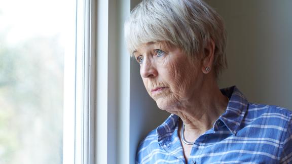 A concerned woman looks out of a window.