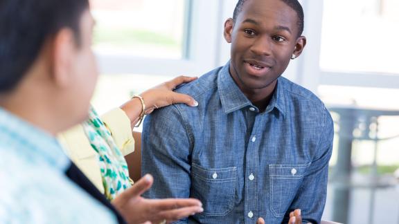 A man in group counselling being comforted.