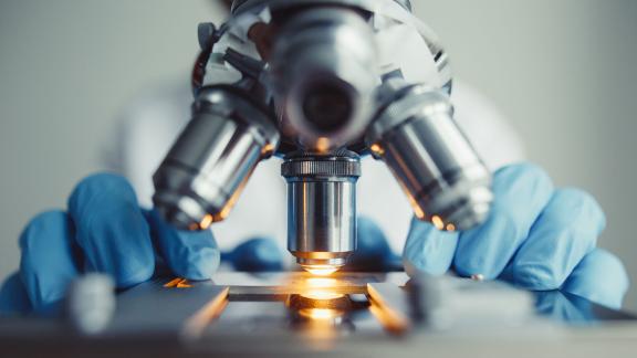 A person wearing gloves, using a microscope.