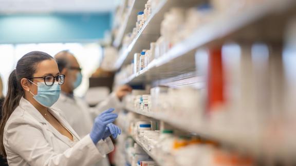 A masked pharmacist checking a shelf.