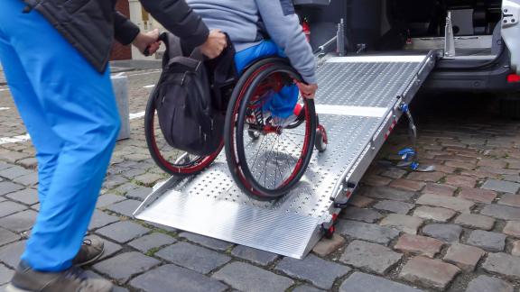 A healthcare worker pushing a wheelchair up a ramp and into a car.