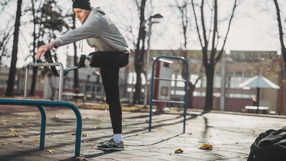 A man with a prosthetic leg stretching in the park.