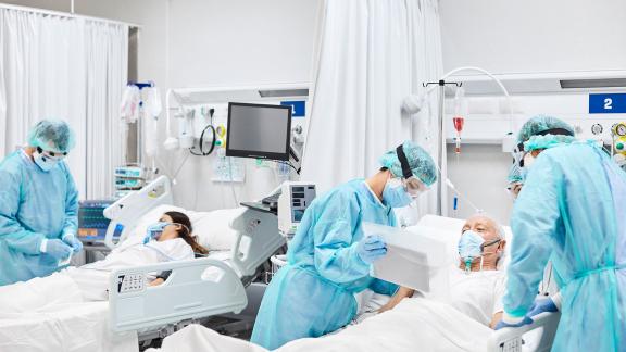 Hospital staff in PPE show an elderly patient his file.