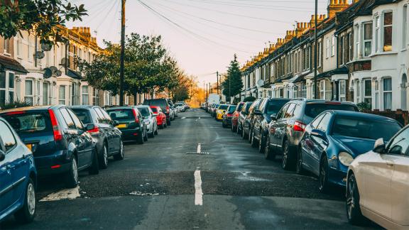 A typical Londoner neighbourhood with 2 storey houses on a long street with cars lining each side of the road in early morning.