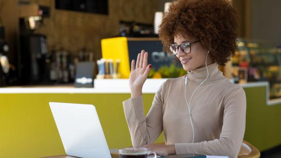 An office worker waving on a video call.