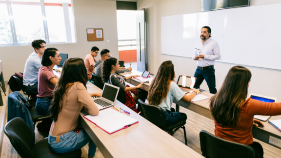 A photo of a group of students, of mixed gender and ethnicities, looking towards a teacher leading a seminar.