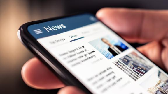 Person holding phone in hand looking at a news feed