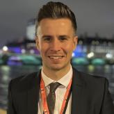 A photo of Joshua Poole, standing at night with the River Thames in the background.