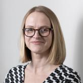 Accessibility description: A photo of Emma Paveley, a white woman with shoulder-length blonde hair, wearing glasses and smiling towards the camera.