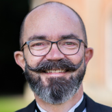 Accessibility description: A photo of Ian Callaghan, a white man with very short dark hair, a beard and large moustache, wearing glasses and smiling towards the camera.