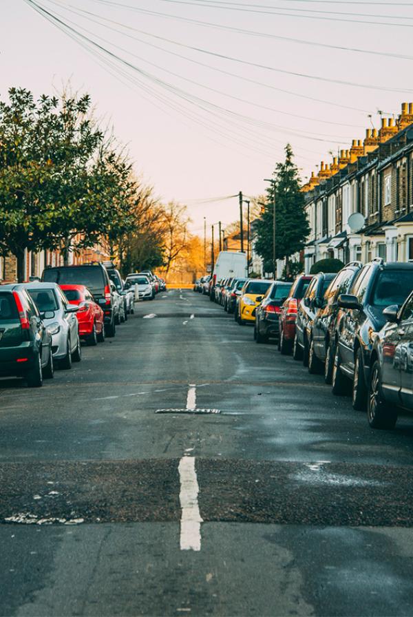 A typical Londoner neighbourhood with 2 storey houses on a long street with cars lining each side of the road in early morning.