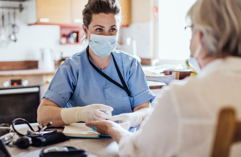 A community nurse in a mask, consulting a patient.