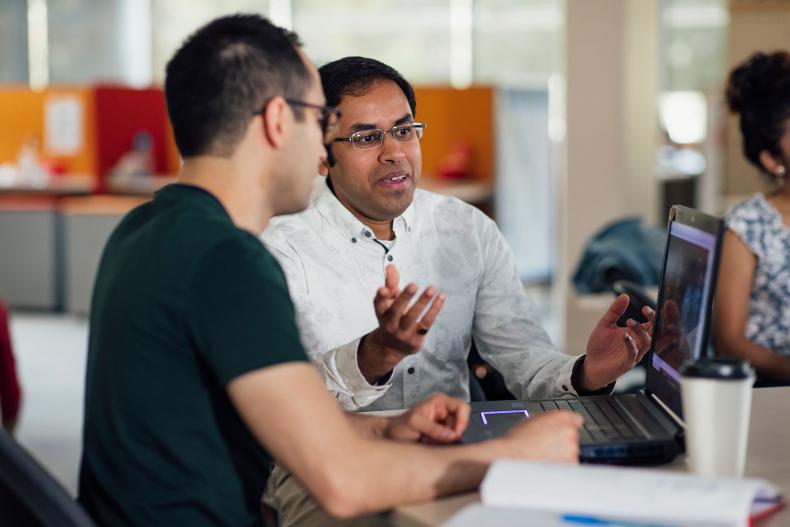 Office workers having a conversation and looking at a laptop.